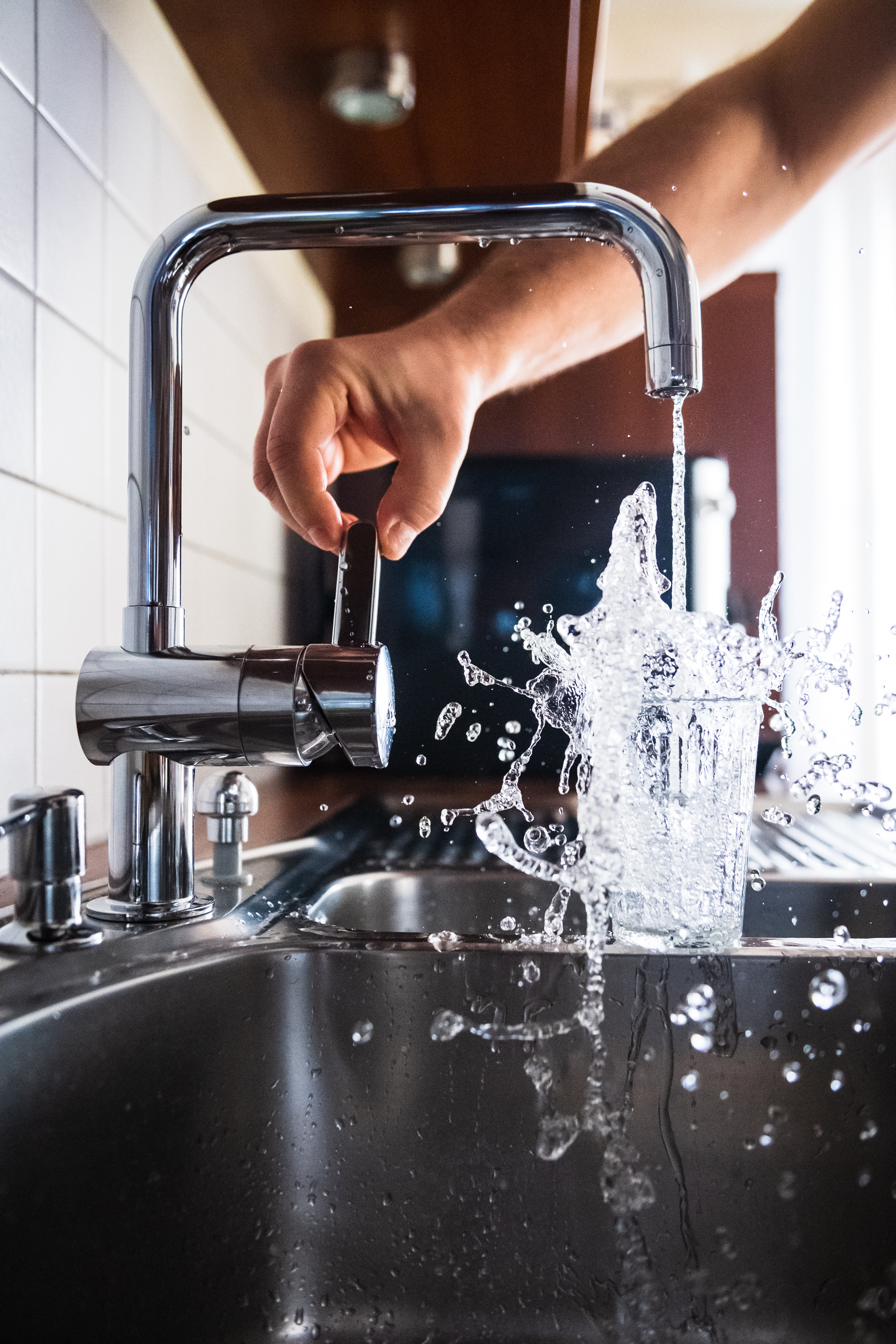 Arm som öppnar blandarkran och vatten rinner ner i ett dricksglas